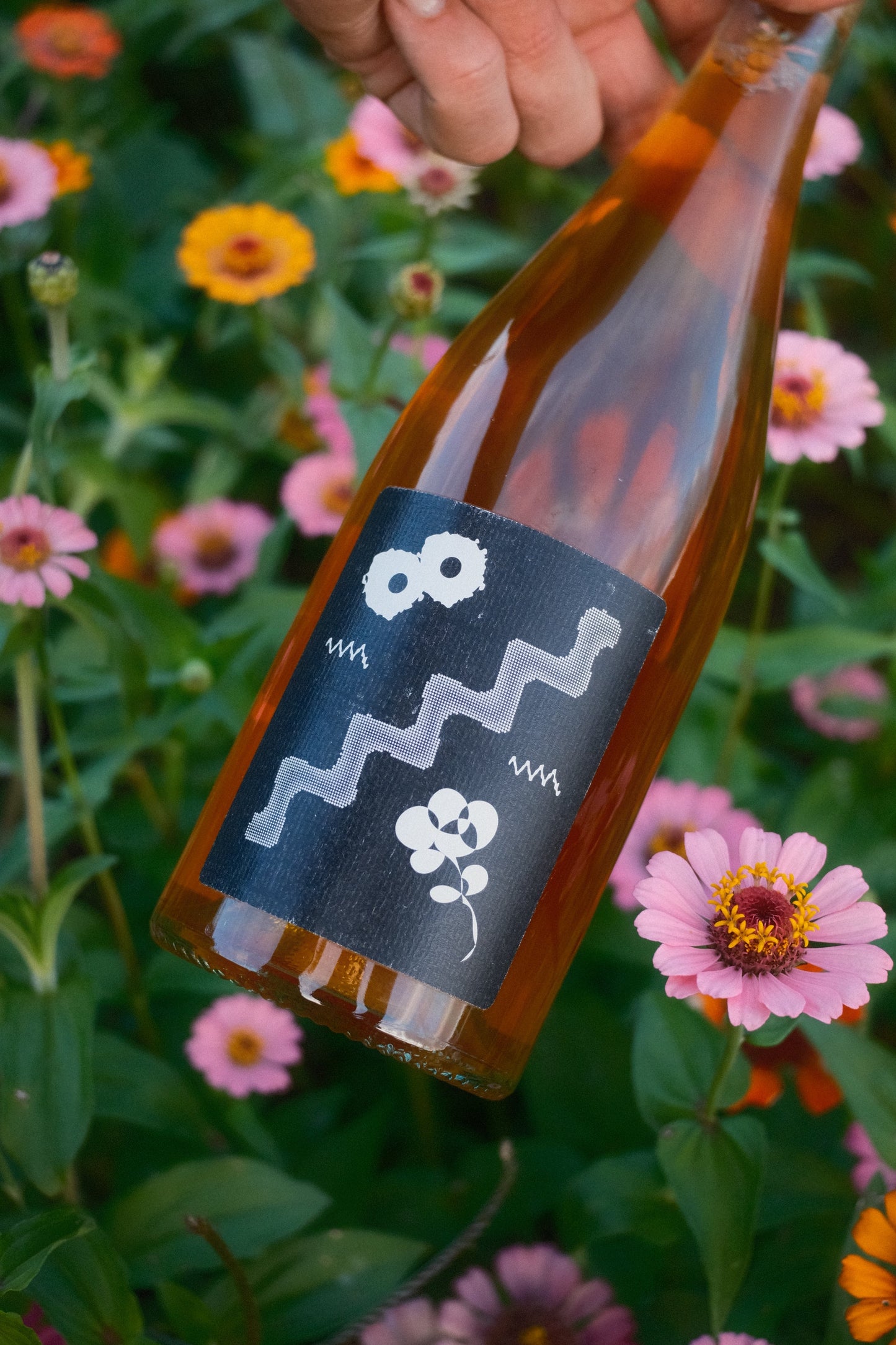 Bottle with a decorative label held in front of flowers